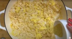 Fried rice with scrambled eggs in a pan, being seasoned with spice mix from a white bowl.